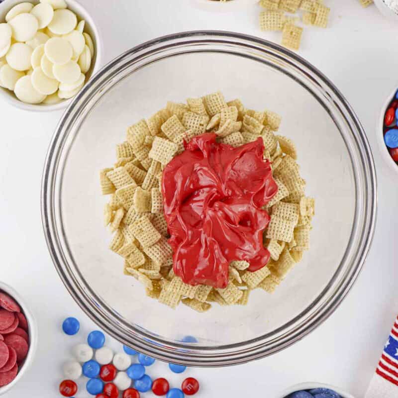 Overhead view of process shot 1 - place 2 cups of the chex in a medium mixing bowl and add the melted red candy melts. Gently mix until the cereal is fully coated.
