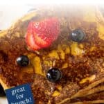 Overhead shot of french toast stacked on a white plate garnished with sliced strawberries, blueberries, and syrup.