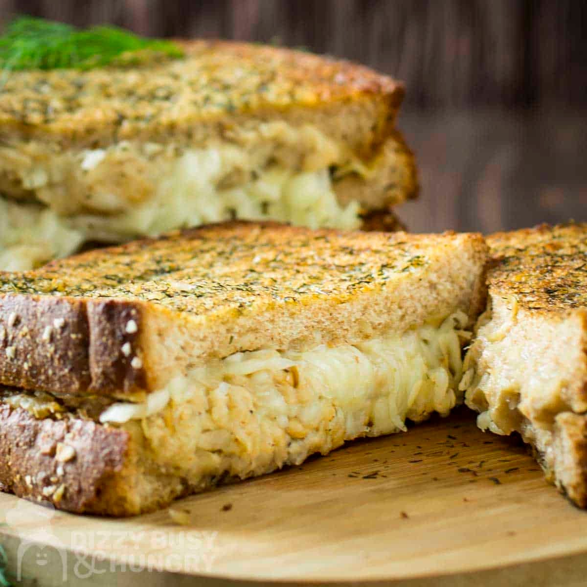Side shot of four grilled cheese halves stacked on a cutting board garnished with fresh dill.