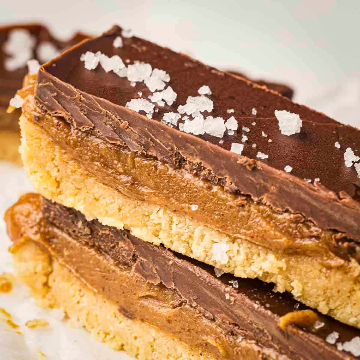 Side shot of two caramel bars sprinkled with flaky salt on a white surface.