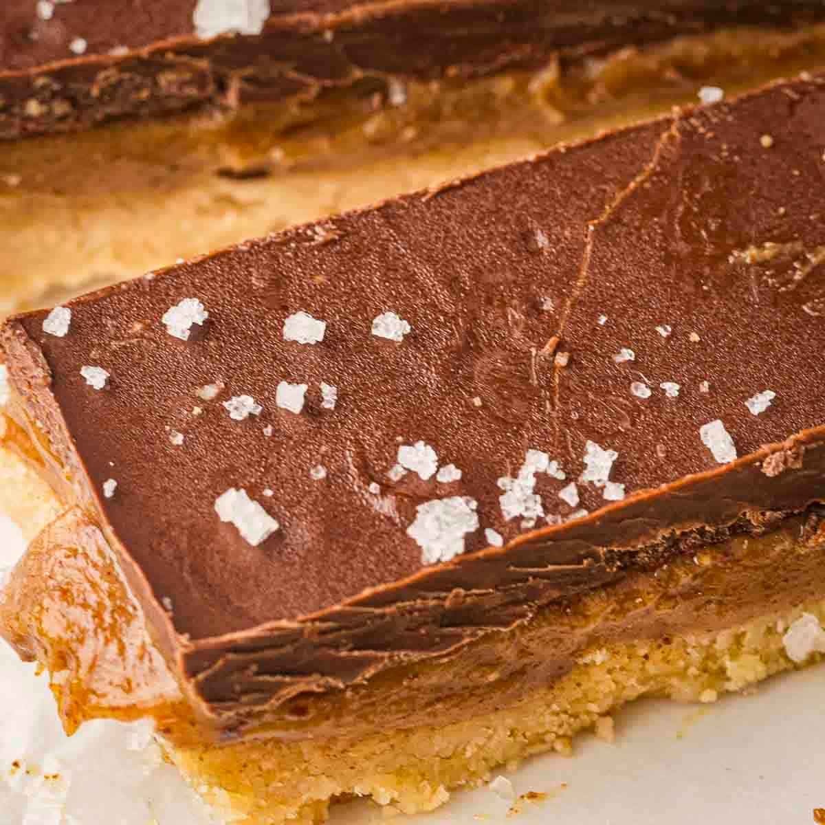 Close up shot of a caramel bar sprinkled with flaky salt on a white surface.