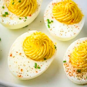 Overhead close up shot of multiple deviled eggs garnished with paprika and chives on a white plate.