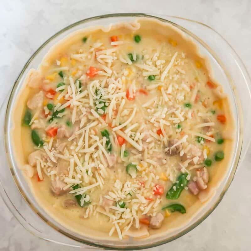 Overhead view of process shot 4 - spray a 1.5 quart casserole dish with cooking spray, and place the first pie crust along the bottom and press the excess up the sides. Pour the chicken mixture onto the crust and spinkle the remaining ½ cup of cheddar cheese.