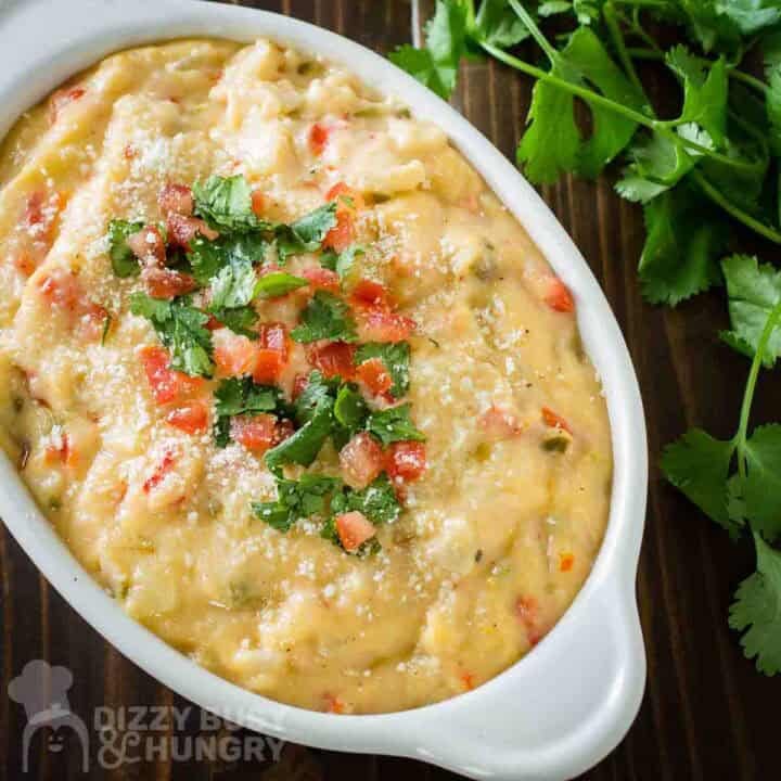 Close up shot of queso dip in a white serving bowl garnished with parsley and diced tomatoes with a bundle of fresh parlsey on the side.