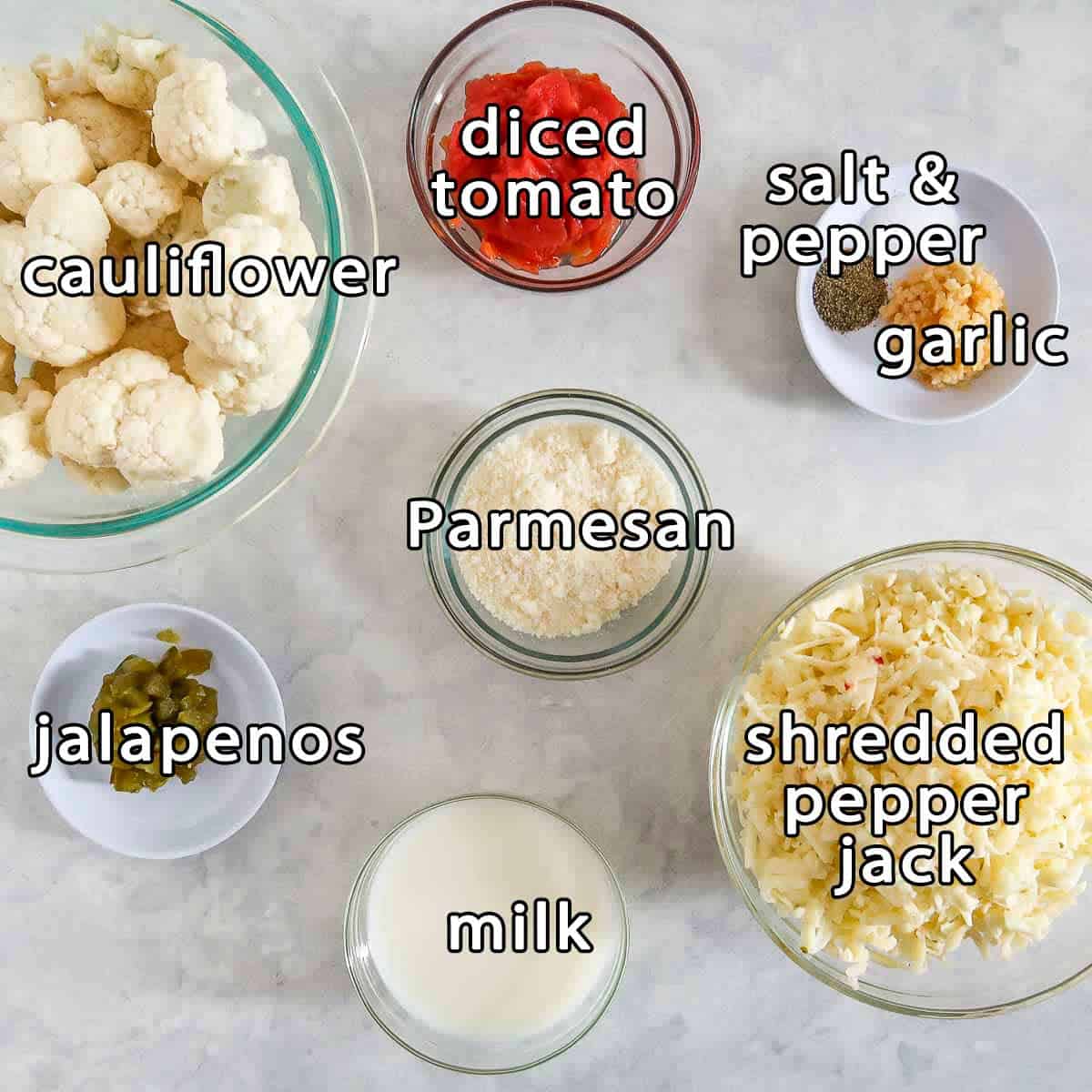 Overhead shot of ingredients - cauliflower, jalapenos, diced tomato, parmesan, shredded pepper jack, milk, garlic, and salt and pepper.