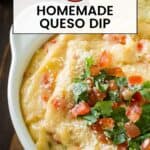 Close up shot of queso dip garnished with parsley and diced tomatoes with a tortilla chip being dipped in.