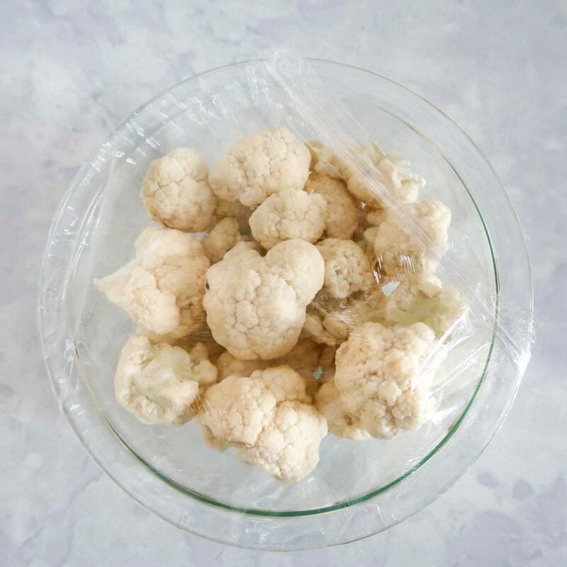 Overhead view of process shot 1 - place the cauliflower florets in a microwaveable bowl, add about 2 tablespoons water, and cover with plastic wrap, and microwave 4-5 minutes until the cauliflower is very tender.