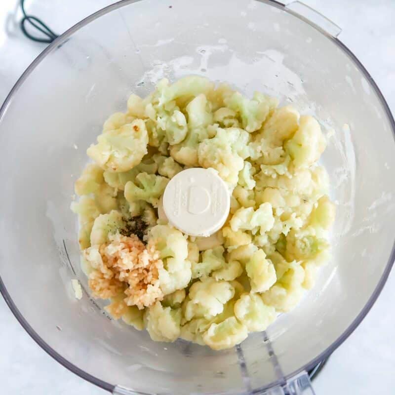 Overhead view of process shot 2 - drain the cauliflower and transfer to a food processor or blender. Add the garlic, milk, salt, and pepper.