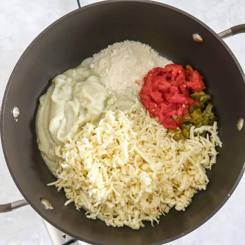 Overhead view of process shot 4 - in a large skillet, place the cauliflower mixture, pepper jack cheese, parmesan cheese, jalapenos, and tomato.