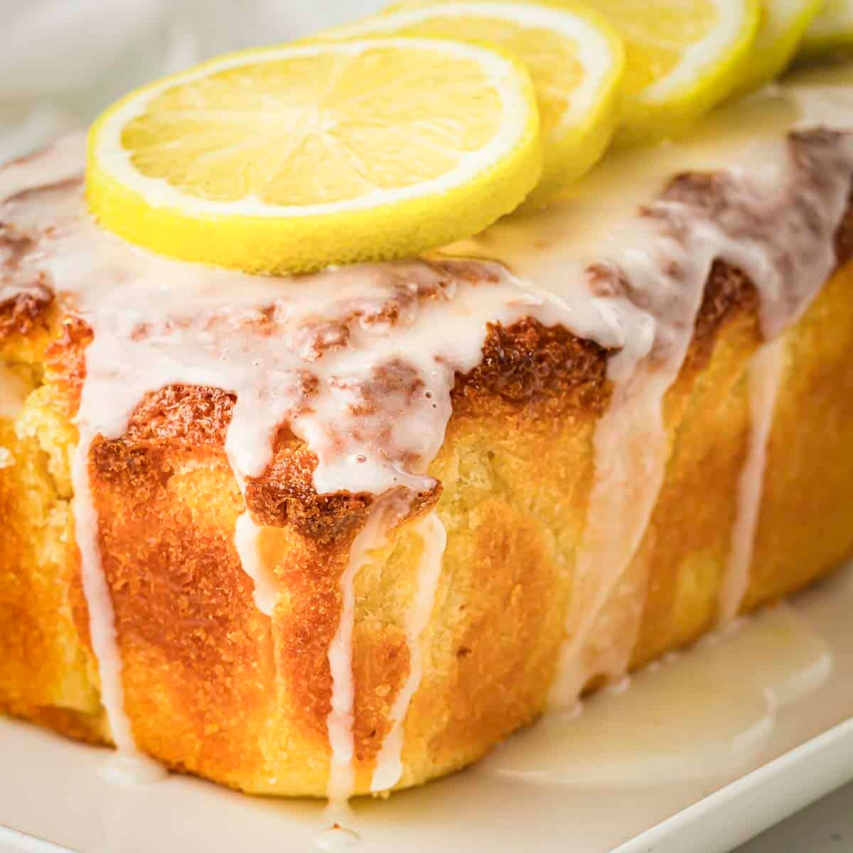 Side shot of lemon loaf cake with lemon glaze garnished with lemon slices.