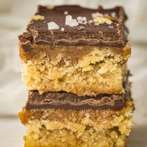 Side shot of two caramel bars stacked on each other sprinkled with flaky salt on a white surface.