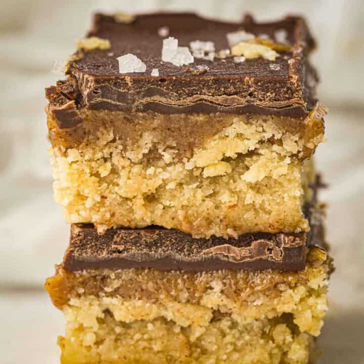 Side shot of two caramel bars stacked on each other sprinkled with flaky salt on a white surface.
