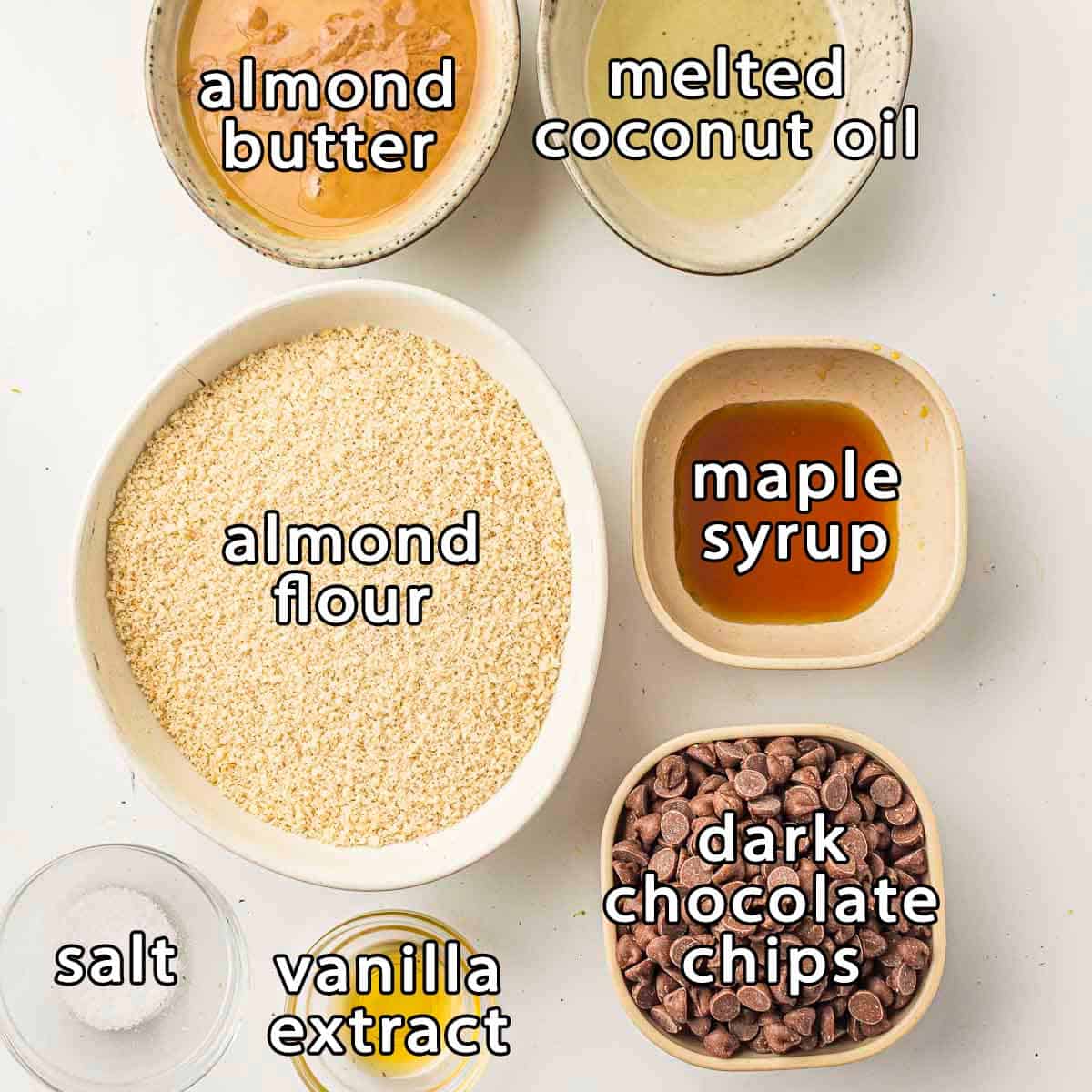 Overhead shot of ingredients - almond butter, melted coconut oil, almond flour, maple syrup, dark chocolate chips, vanilla extract, and salt.