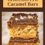 Side shot of two caramel bars stacked on each other sprinkled with flaky salt on a white surface.