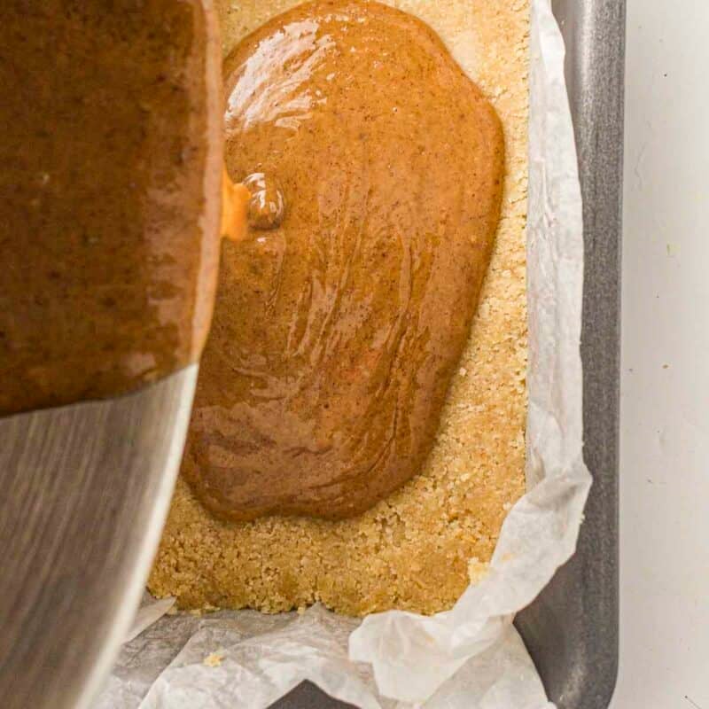 Overhead view of process shot 3 - in a separate bowl, stir together almond butter, maple syrup, melted coconut oil and salt until smooth. Spread caramel layer evenly over the chilled base. Refrigerate for 30-40 minutes until set.