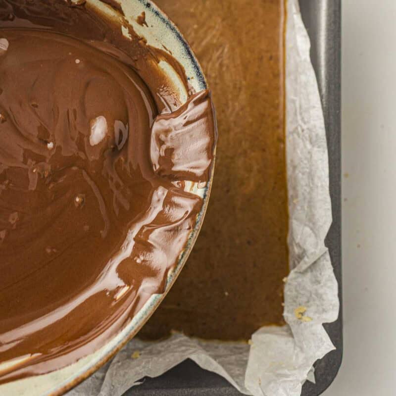 Overhead view of process shot 4 - melt chocolate chips with coconut oil in the microwave in 20 second intervals, stirring between each, until smooth. Pour melted chocolate over the caramel layer and spread evenly. Sprinkle with flaky salt if using.