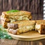 Side shot of four grilled cheese halves stacked on a cutting board garnished with fresh dill.