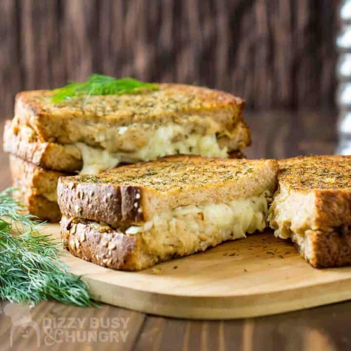 Side shot of four grilled cheese halves stacked on a cutting board garnished with fresh dill.