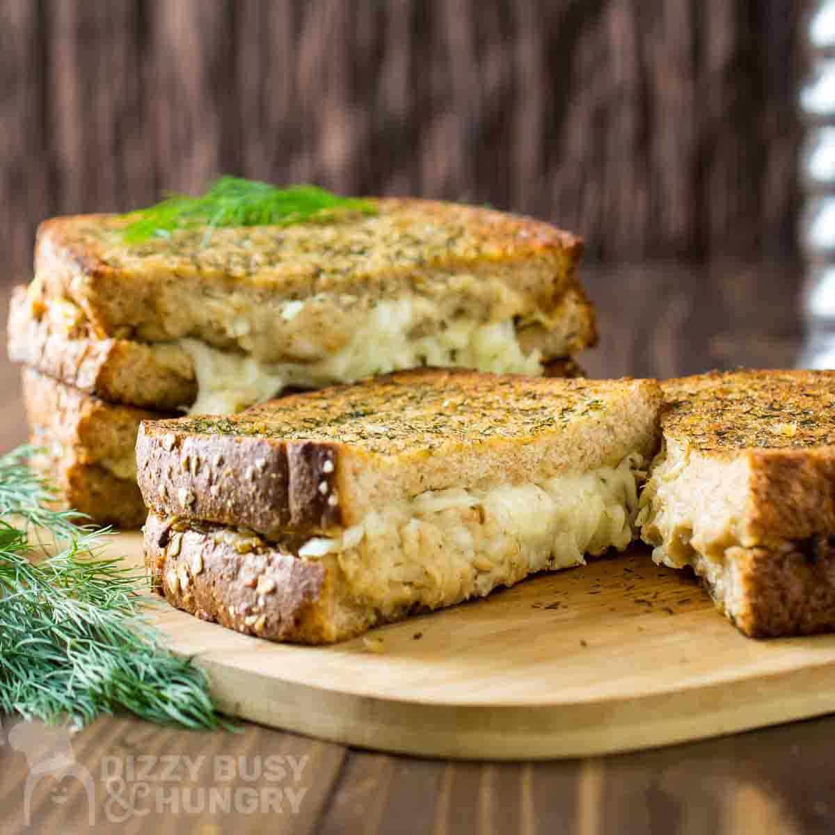 Side shot of four grilled cheese halves stacked on a cutting board garnished with fresh dill.