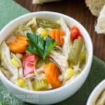 Close up shot of chicken soup with a sprig of fresh parsley in a white bowl on a green cloth.