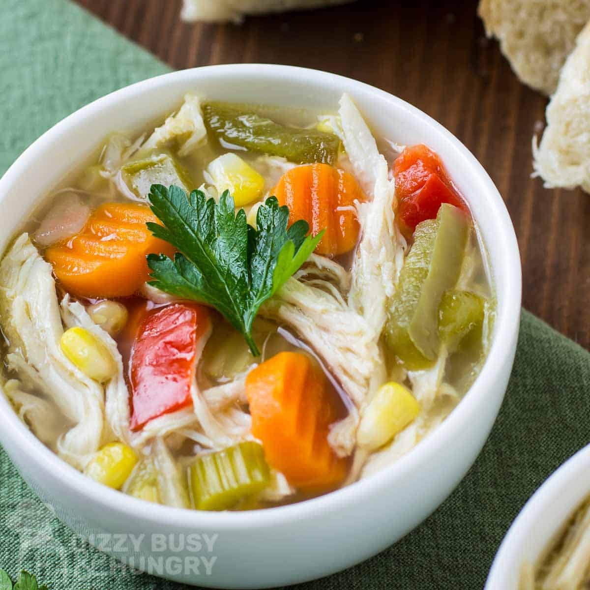 Close up shot of chicken soup with a sprig of fresh parsley in a white bowl on a green cloth.