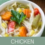 Close up shot of chicken soup with a sprig of fresh parsley in a white bowl on a green cloth.