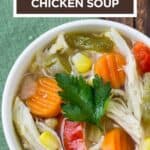 Close up shot of chicken soup with a sprig of fresh parsley in a white bowl on a green cloth.