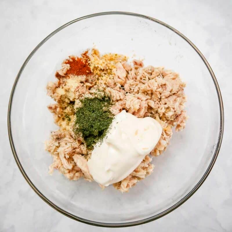 Overhead view of process shot 1 - make the tuna salad by combining the tuna, mayonnaise, dill, onion flakes, garlic powder and paprika in a medium bowl.