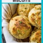 Overhead shot of golden brown biscuits garnished with chives in a bowl wrapped in a white striped cloth with a wooden spoon on the side.