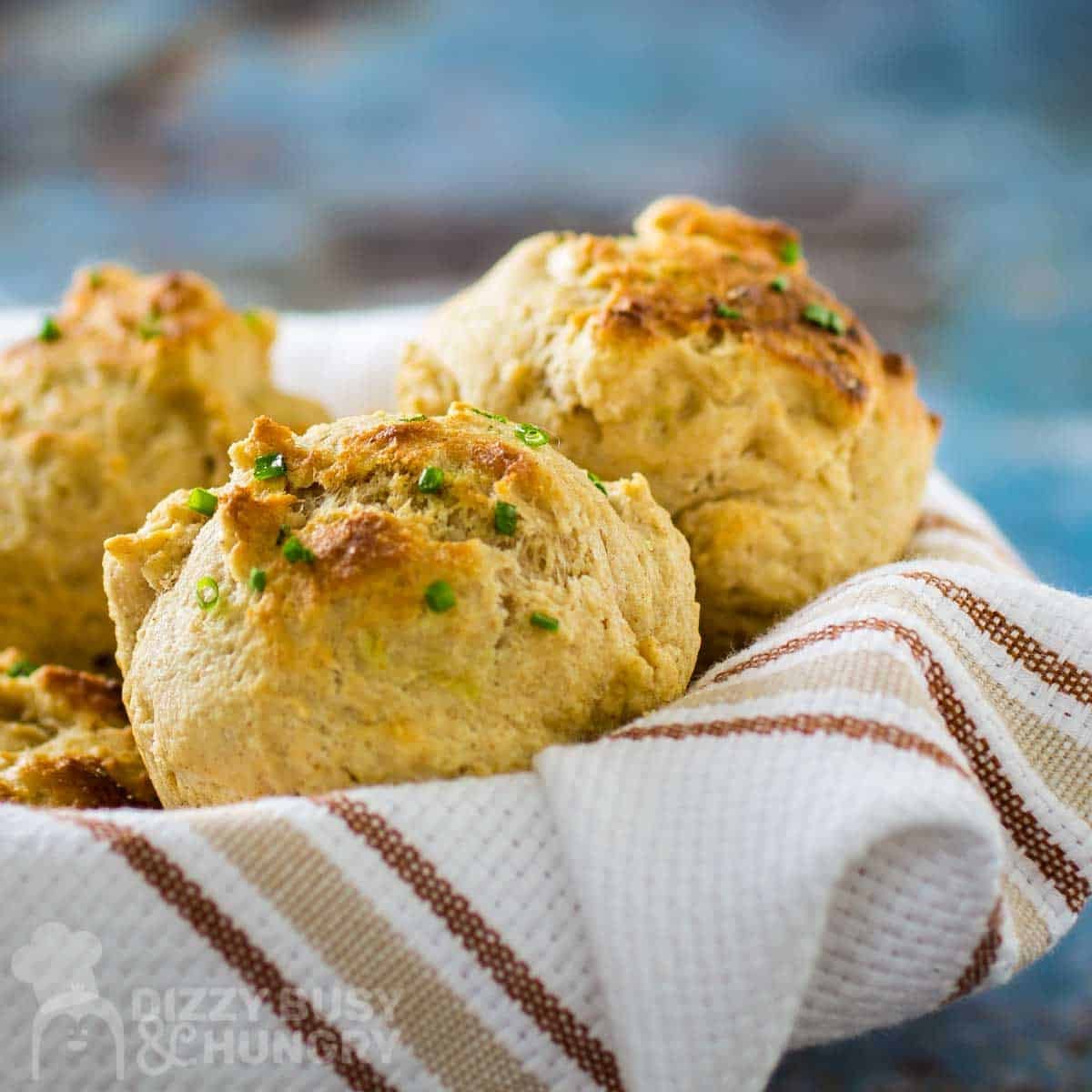 Side shot of golden brown biscuits garnished with chives in a bowl wrapped in a white striped cloth.