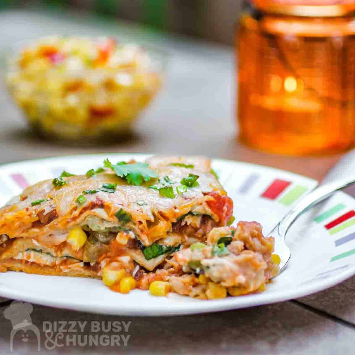 Side view of vegetarian Mexican lasagna garnished with green onions on a colored plate.