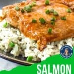 Side shot of glazed salmon on a bed of rice garnished with fresh green onions in a black bowl.