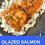 Close up overhead shot of glazed salmon on a bed of rice garnished with fresh green onions in a black bowl.