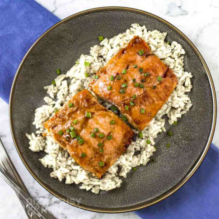 Overhead shot of glazed salmon on a bed of rice garnished with fresh green onions in a black bowl.