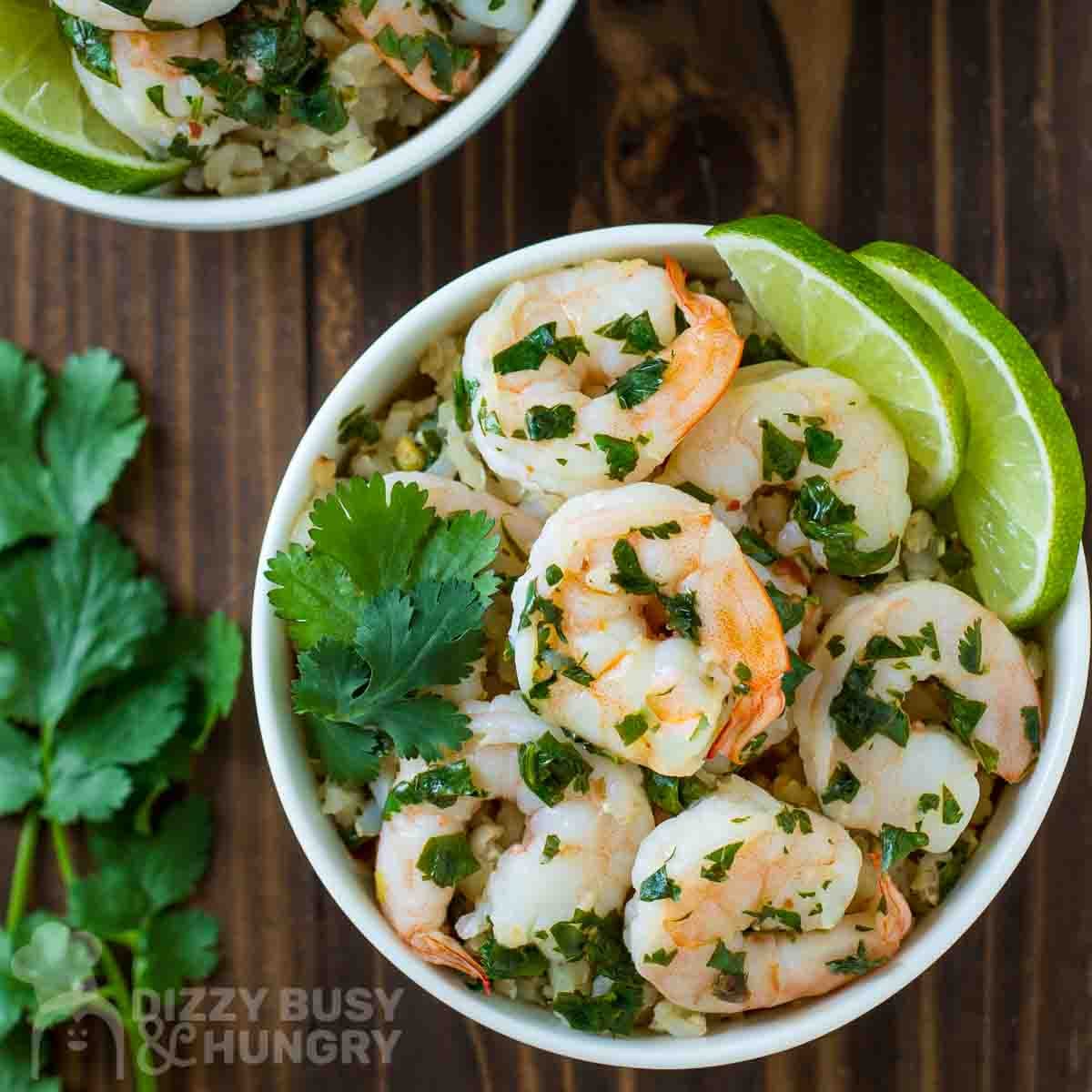 Overhead shot of butter lime shrimp garnished with fresh parsley and lime wedges in a white bowl with parsley sprigs on the side.