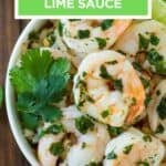 Overhead shot of butter lime shrimp garnished with fresh parsley and lime wedges in a white bowl on a wooden surface.