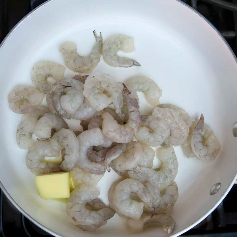Overhead view of process shot 1 - heat a large skillet over medium high heat. Add 2 tablespoons of butter and the shrimp.