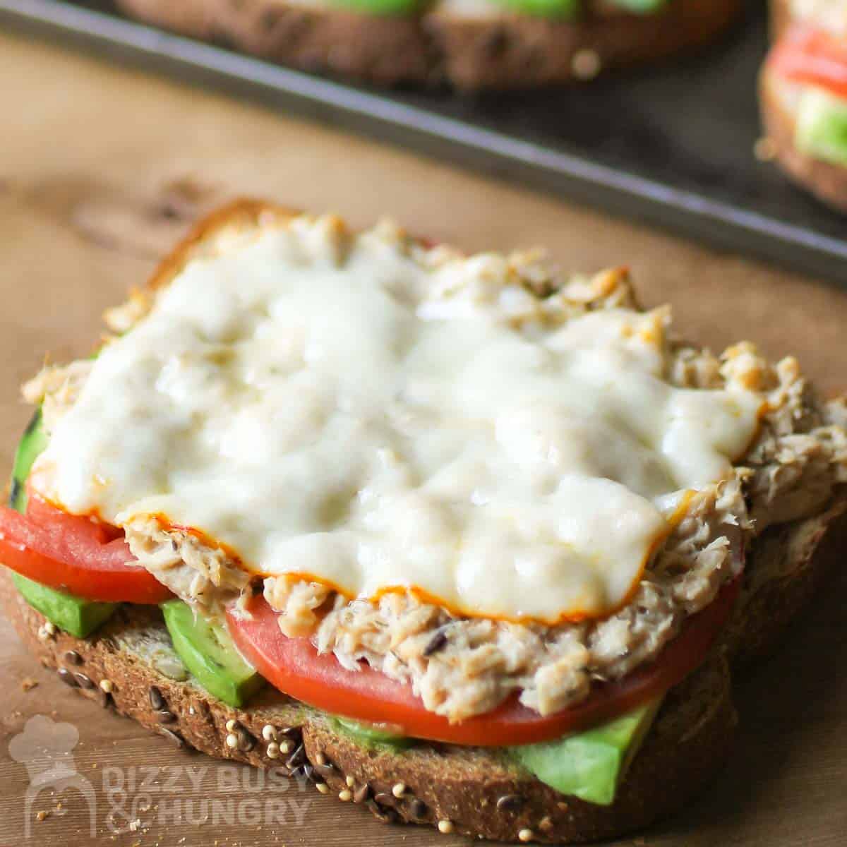 Side close up shot of tuna melt with avocado on a wooden surface with a baking sheet in the background.