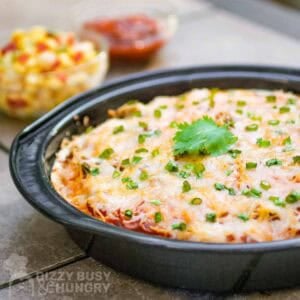 Side view of fiesta lasagna garnished with chives and parsley in a circle metal baking dish.