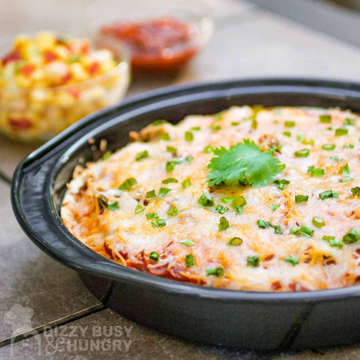 Side view of fiesta lasagna garnished with chives and parsley in a round metal baking dish.