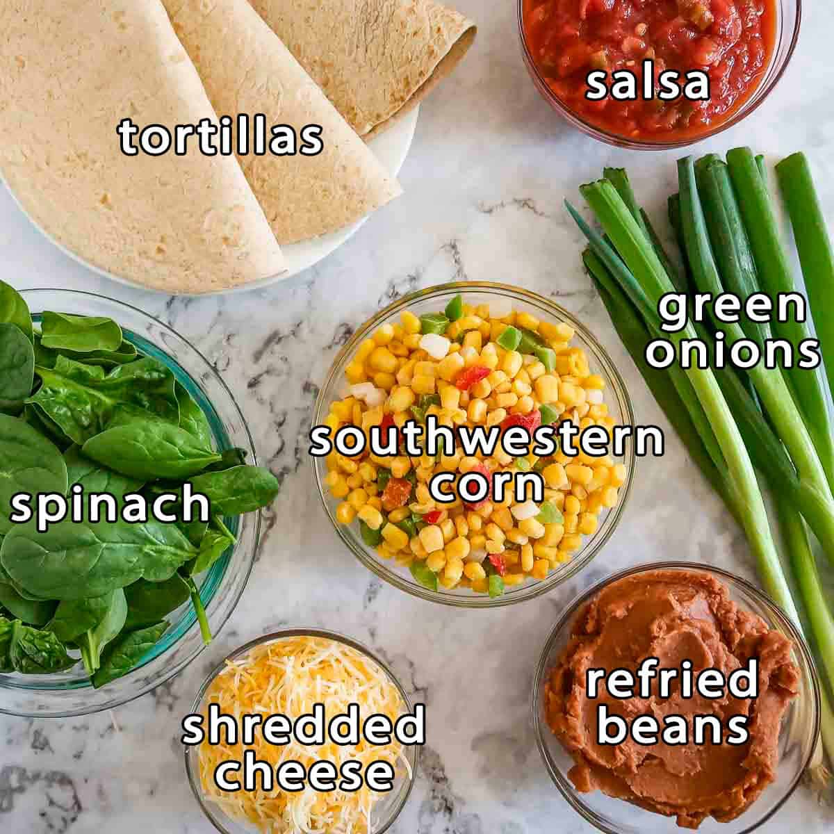 Overhead view of ingredients - tortillas, salsa, green onions, southwestern corn, spinach, refried beans, and shredded cheese.