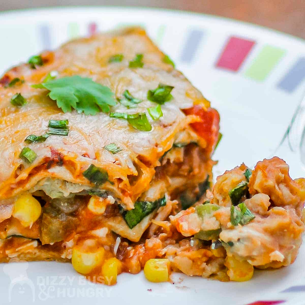Side view of vegetarian Mexican lasagna garnished with green onions on a colored plate.