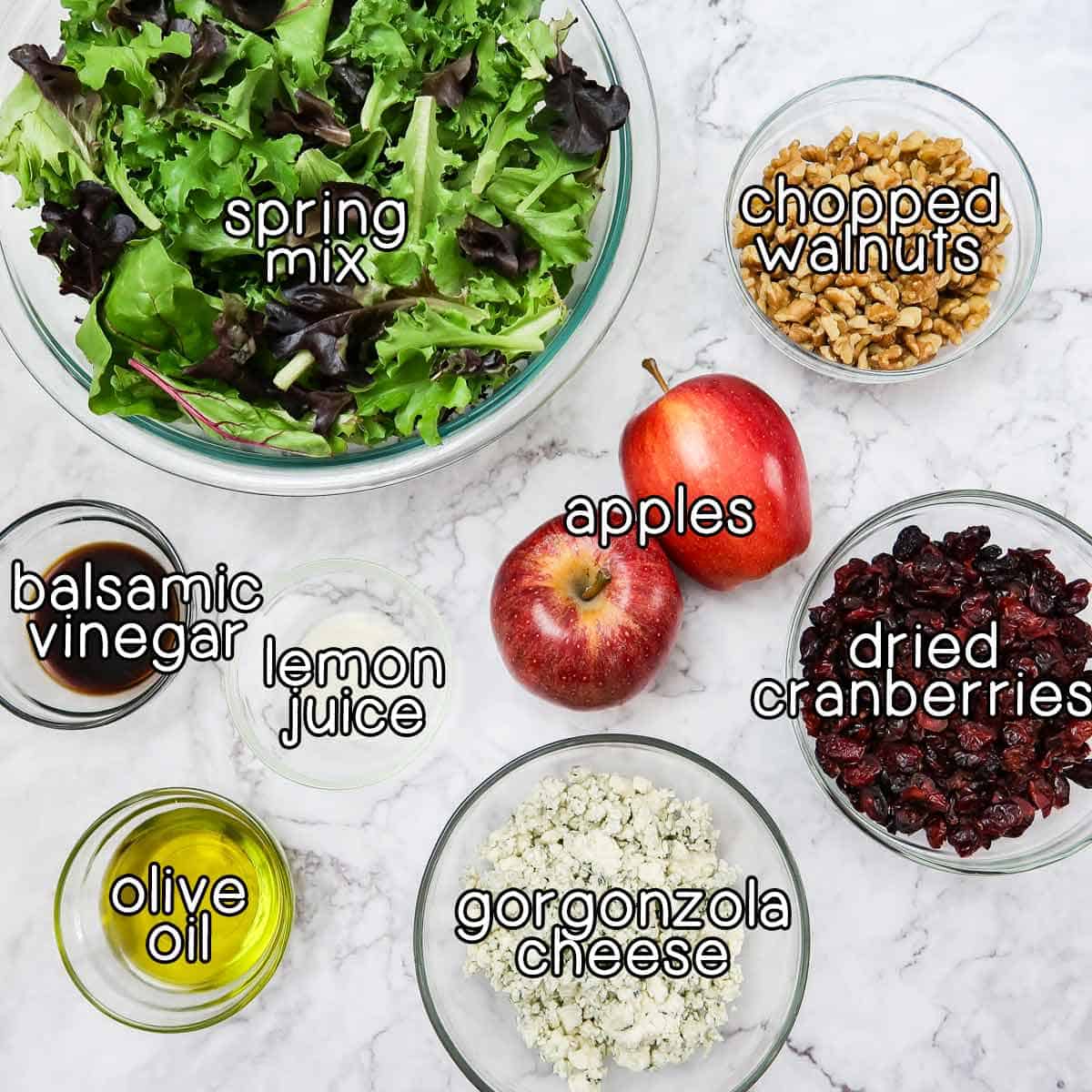 Overhead shot of ingredients - spring mix, chopped walnuts, apples, dried cranberries, balsamic vinegar, lemon juice, olive oil, and gorgonzola.