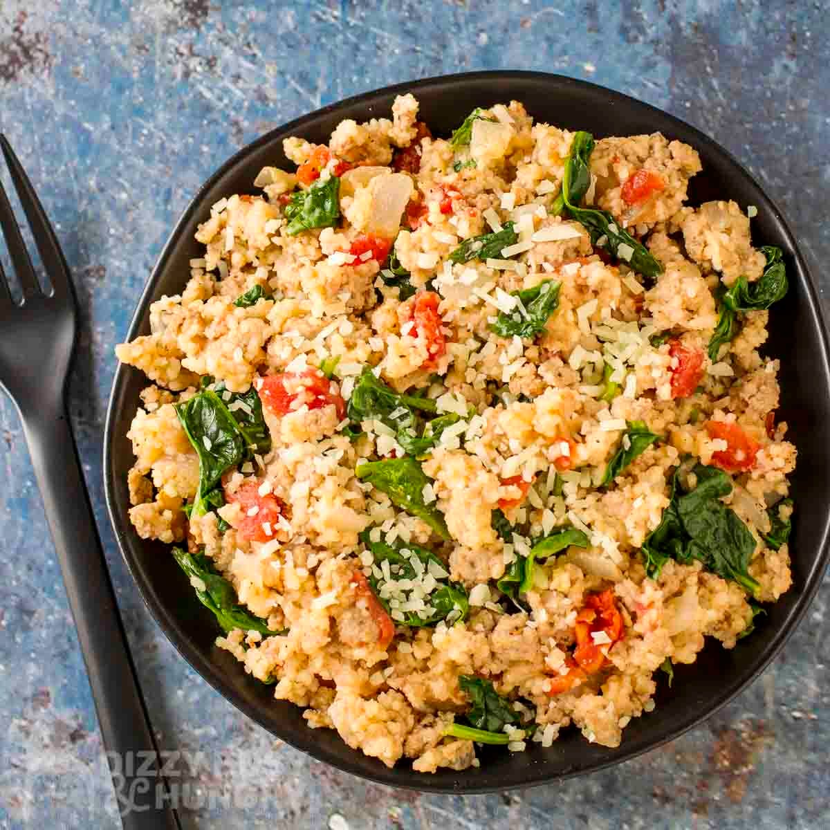 Overhead shot of couscous and ground turkey on a black plate with a black fork on the side.