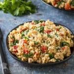 Side shot of couscous and ground turkey on a black plate with fresh herbs in the background.