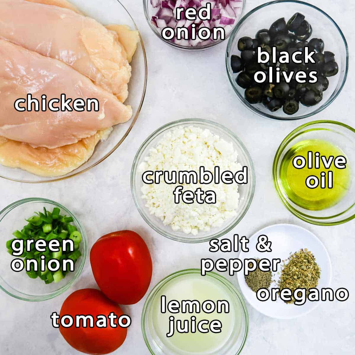 Overhead shot of ingredients - chicken, red onion, black olives, crumbled feta, olive oil, green onions, tomato, lemon juice, oregano, and salt & pepper.