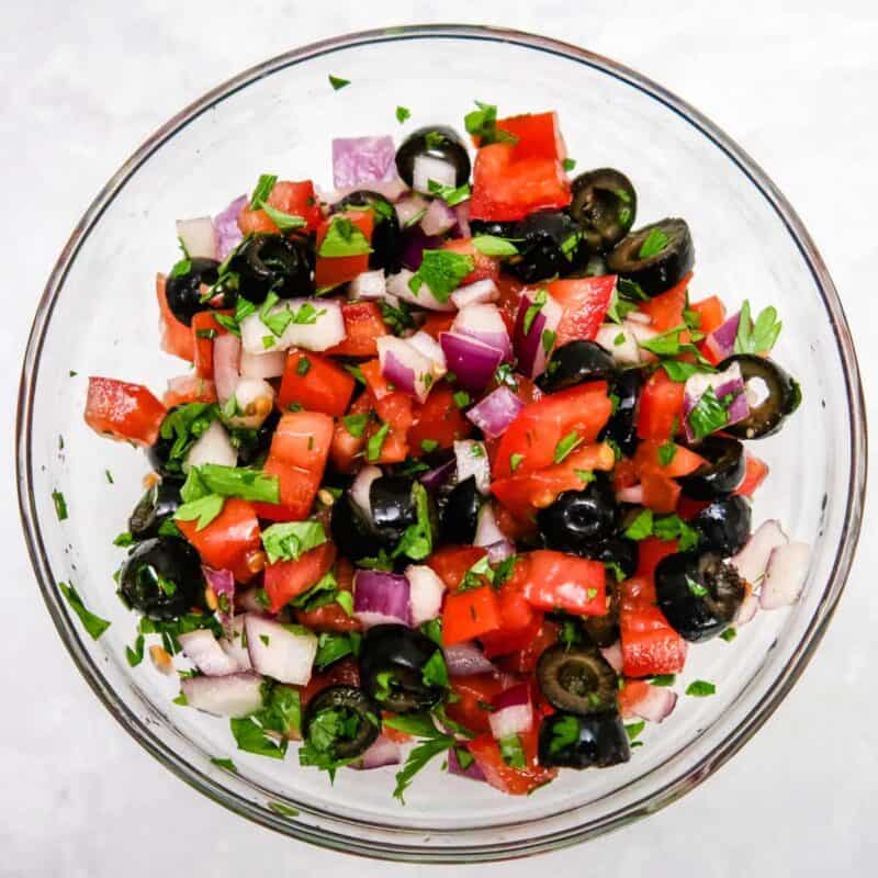 Overhead view of process shot 3 - combine the tomato, onion, olives, and parsley to make the mediterranean-style salsa.