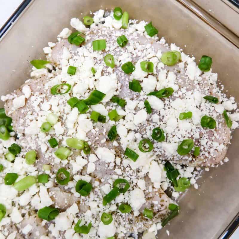 Overhead view of process shot 4 - place the chicken in a baking dish, top with the feta and green onions, and place in the oven.