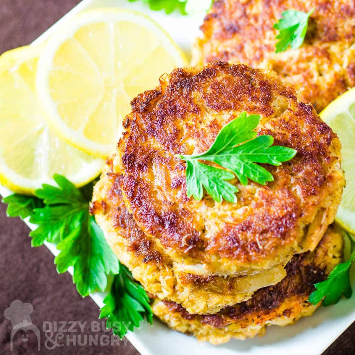 Close up shot of crab cakes stacked on a bed of lemon slices garnished with fresh herbs.