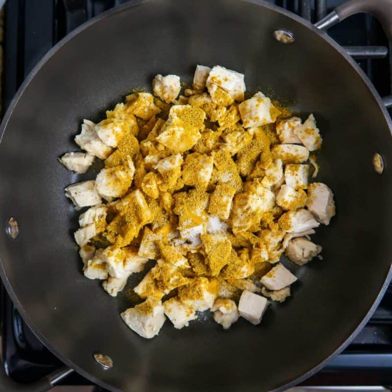 Overhead view of process shot 1 - place the chicken pieces in a large skillet and heat over medium heat. Sprinkle with curry powder and salt.